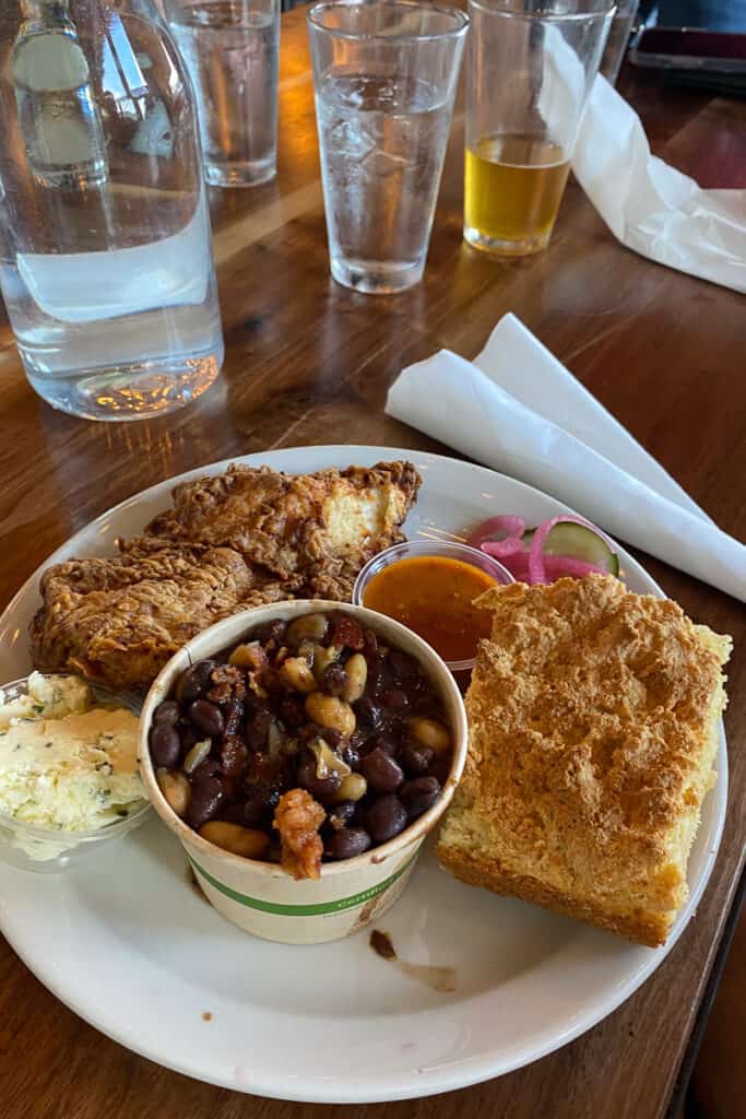Plate of apricot glazed fried chicken, corn grits bread, and baked beans.