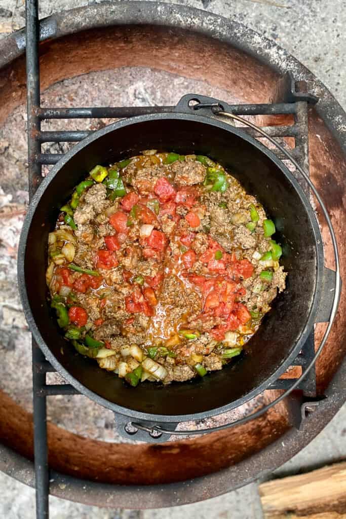 Meat, green peppers, tomatoes and onions in Dutch oven over campfire.