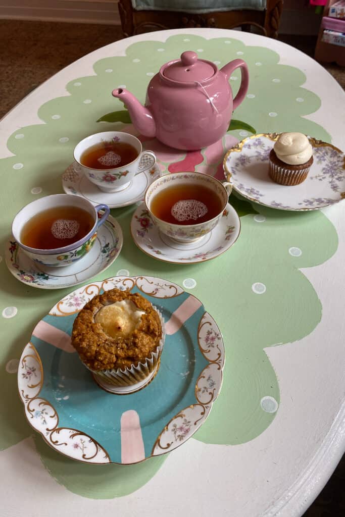 Pumpkin cream cheese muffin, caramel pumpkin cupcake, three cups filled with peaches and ginger tea, and pink teapot.