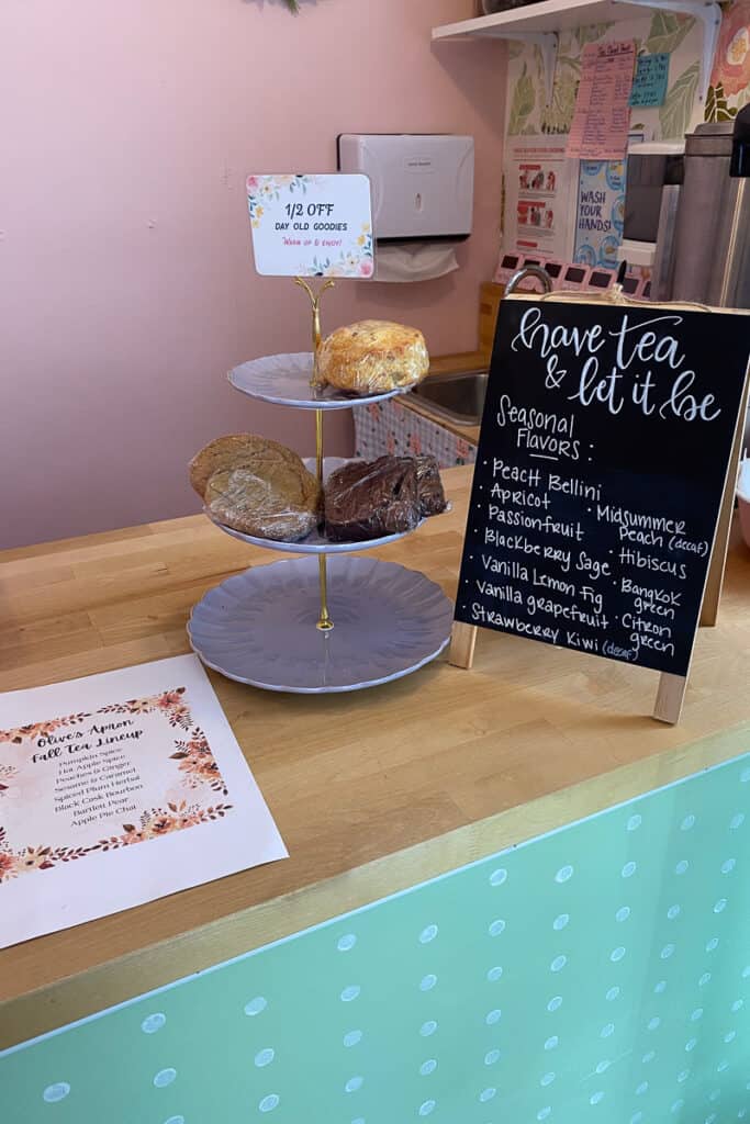 Lists of seasonal teas at Olive's Apron Bakery and Tea Shop, along with platter of day-old baked goods for sale.