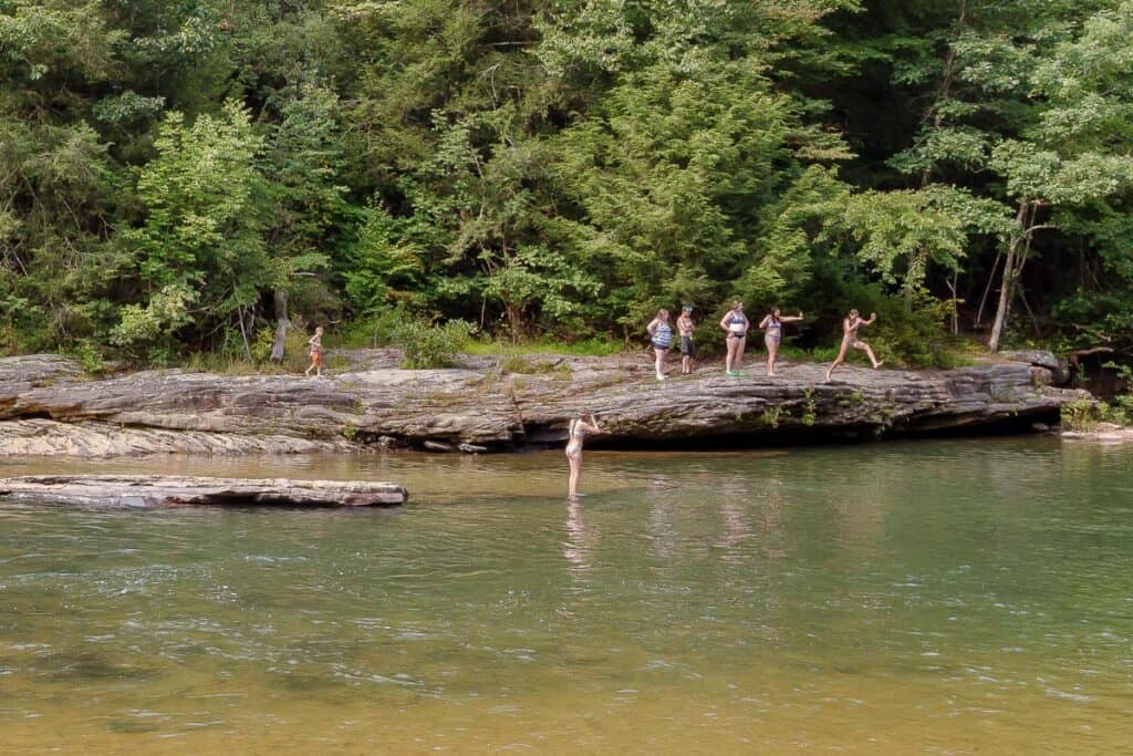 People jumping from rocky ledge into river at Audra State Park.