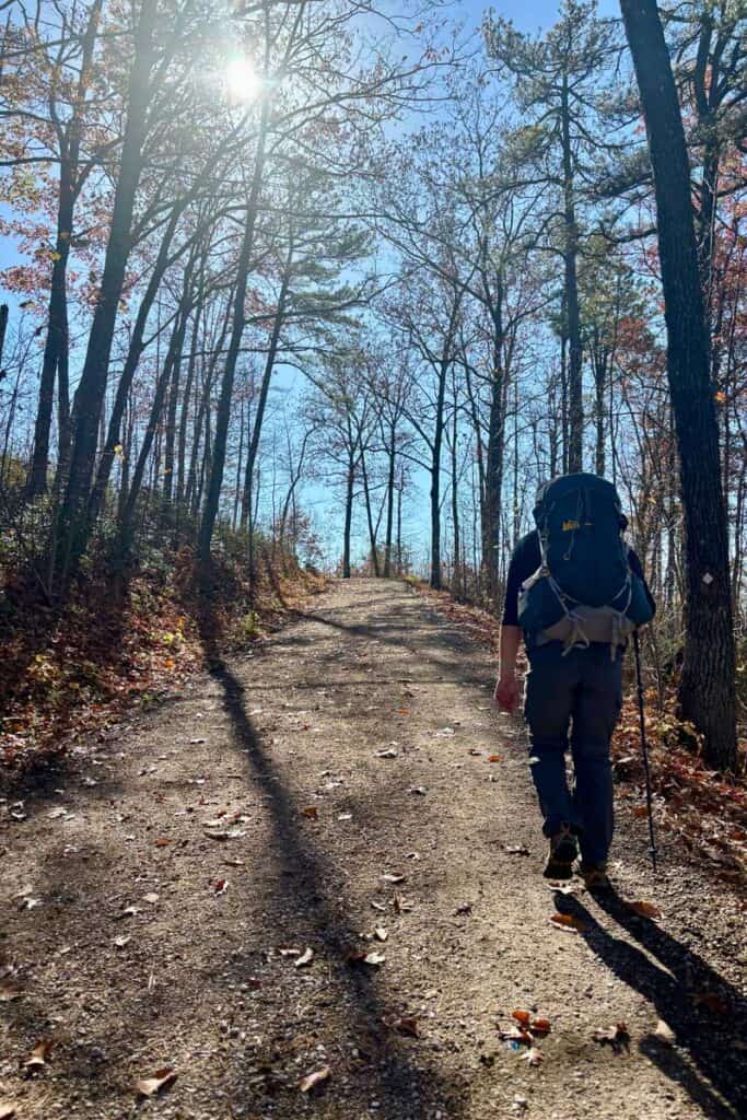 Hiker with backpack climbing uphill gravel trail.