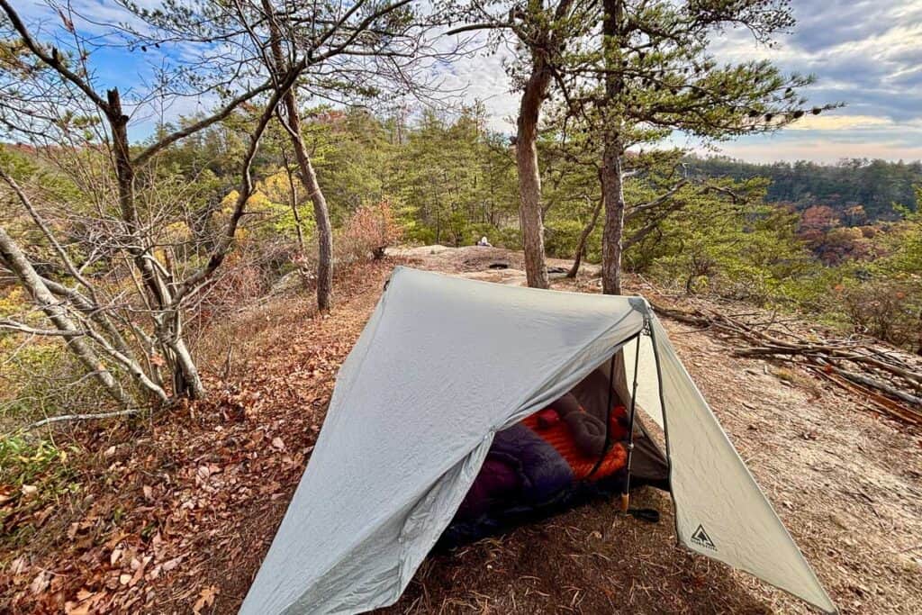 Tent with sleeping pad and quilt visible and trees in background.