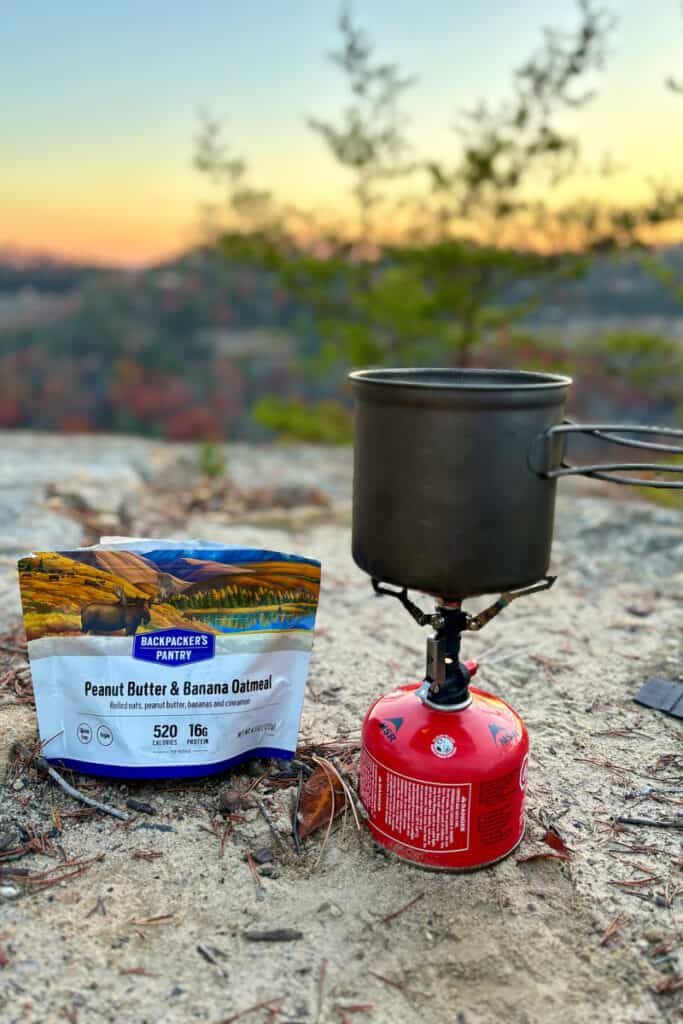 Backpacking stove and packet of oatmeal with sunrise in background.
