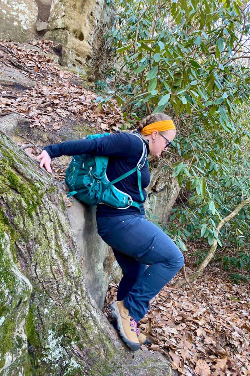 Woman wearing Kuhl hiking pants and scrambling down rocks on trail.