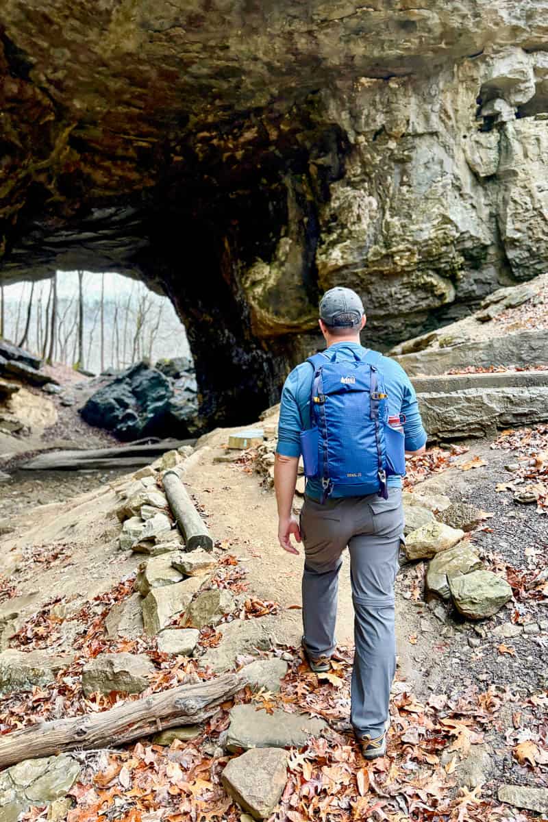Man wearing REI 25 Trail backpack hiking towards rock arch.