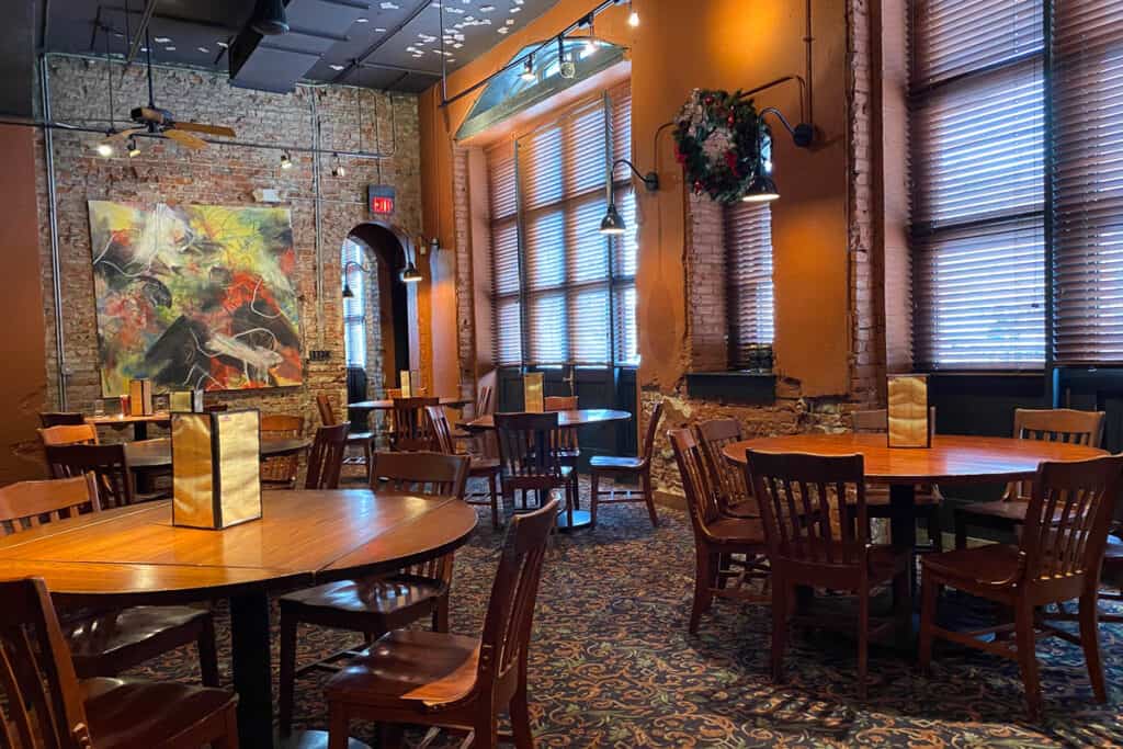 Tables and chairs in carpeted dining room with brick walls.