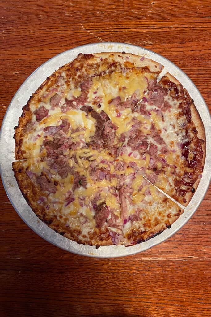 Barbeque pizza with pork, red onions, cheese and sauce.