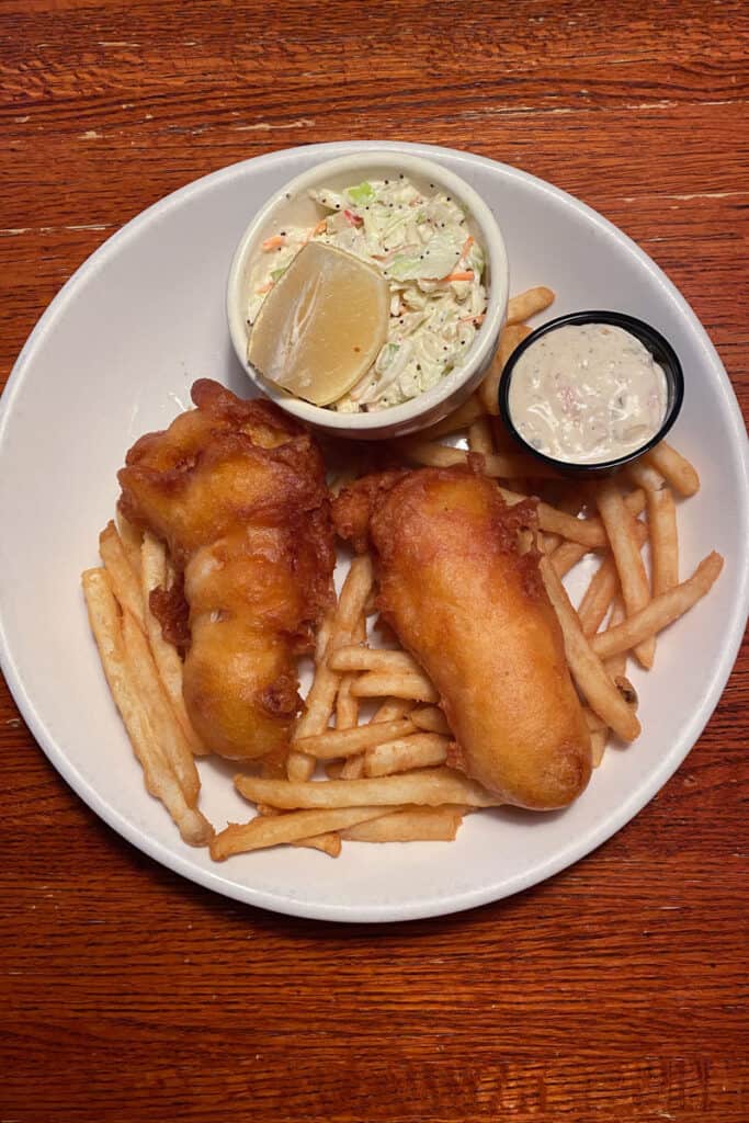Fried fish and fries next to small basins of apple slaw and tartar sauce.
