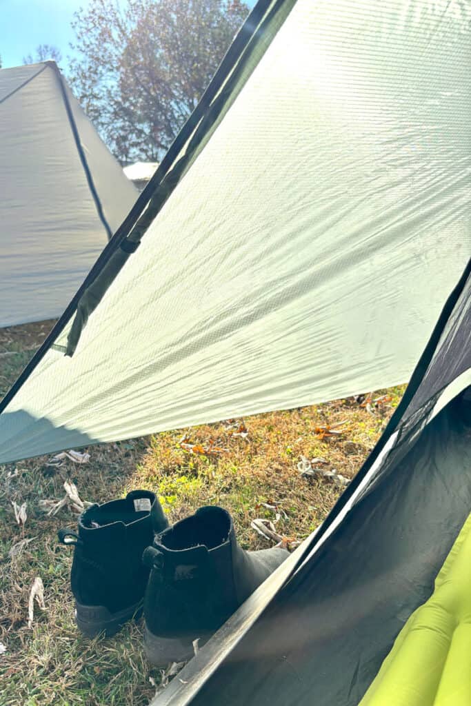Boots set outside ultralight tent with tarp shelter attached to ground.