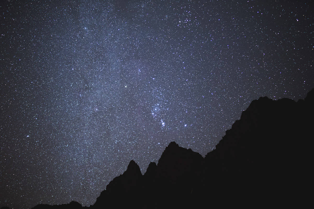 Star-filled sky above silhouetted mountains.