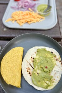 A plate with crunchy taco shell next to flour tortilla spread with guacamole.