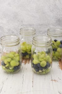 Grapes, blueberries and diced kiwi in jars.