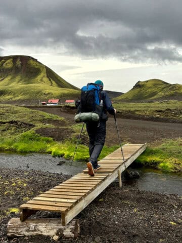 Backpacker crossing small wooden bridge over stream on Laugavegur Trail.