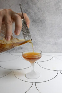 Pouring manhattan cocktail from strainer into coupe glass.