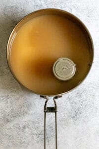 Apple cider in pan with mulling spices steeping from small infuser.
