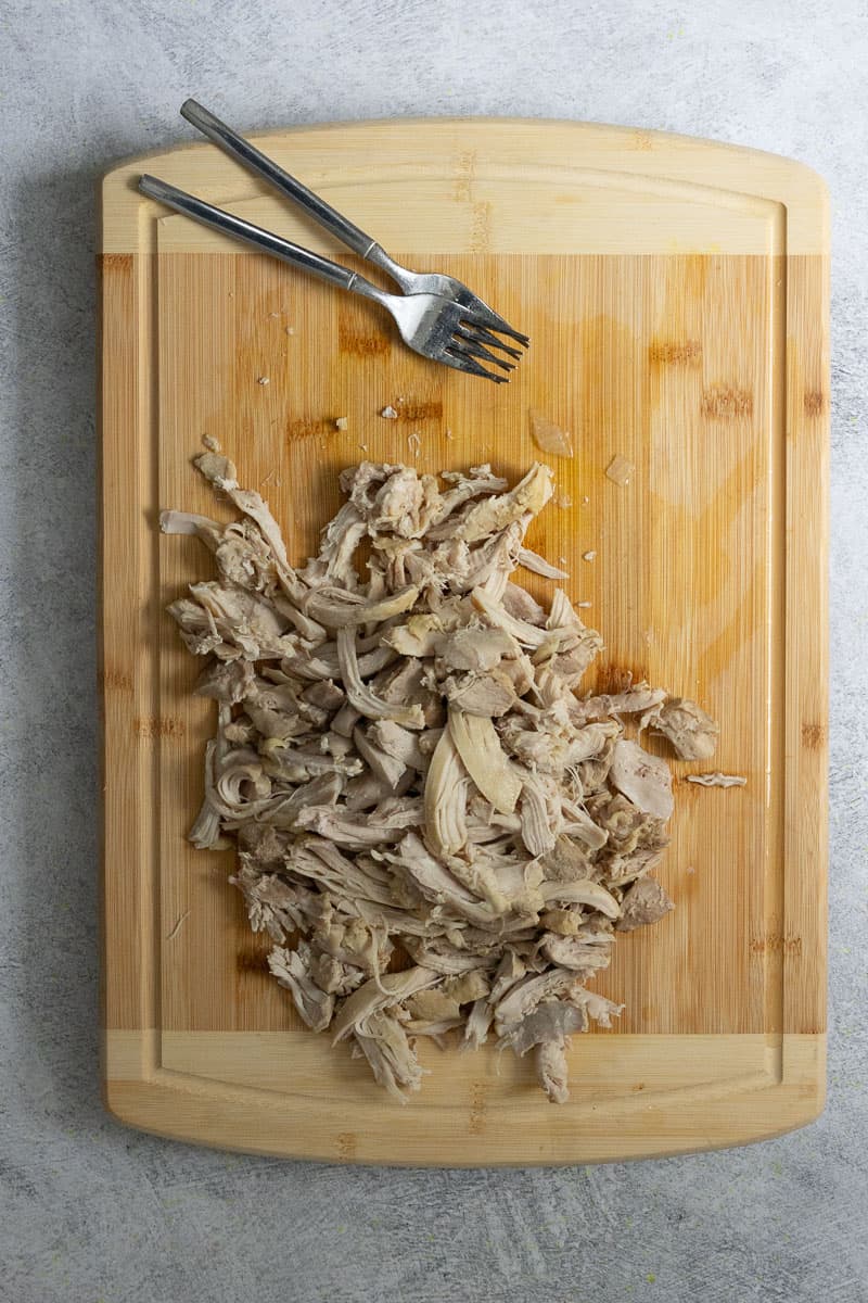 Chicken pulled into strips on cutting board.