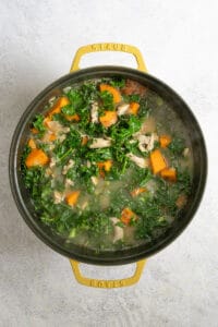 Kale, sweet potatoes and chicken in broth in soup pot.