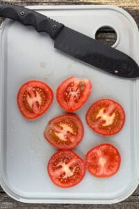 Tomato slices and knife on cutting board.