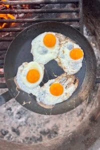 Eggs being fried in skillet for campfire breakfast sandwich.