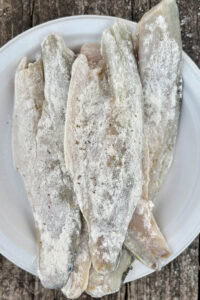 Multiple fish fillets dusted with flour and herbs on paper plate.