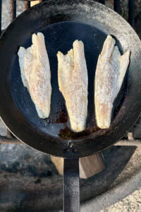 Fish cooking in cast-iron skillet.