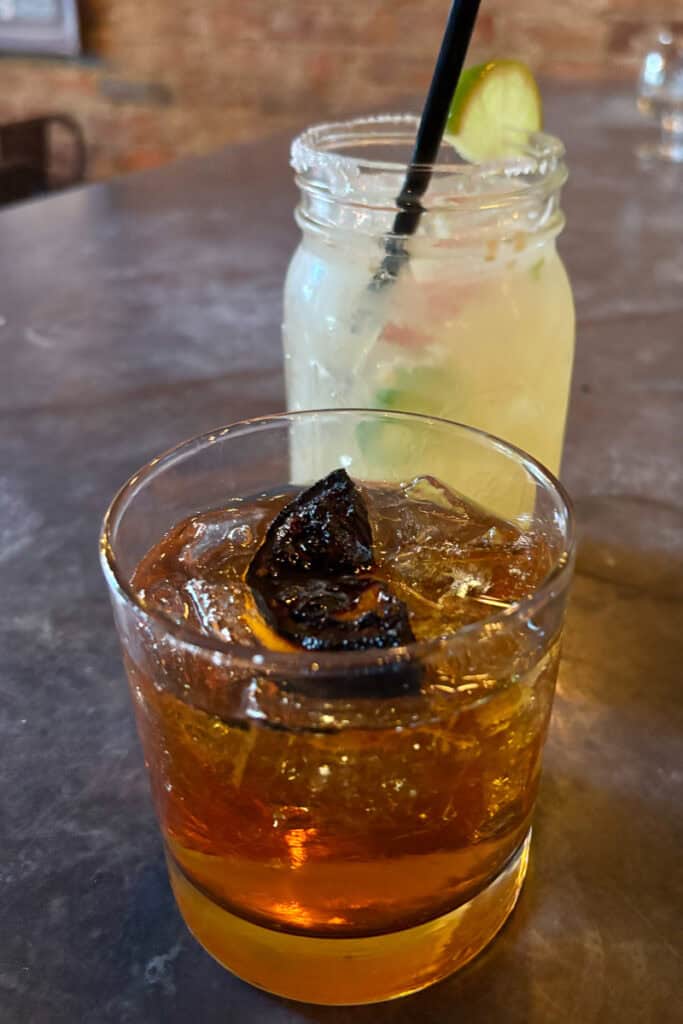 Caballero old fashioned cocktail with mezcal margarita in background.