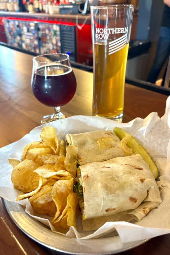Wrap and chips on platter next to two glasses of beer.