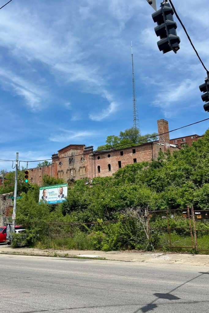 Large dilapidated brick building on hillside as seen from street below, a part of a Cincinnati underground brewery tour.