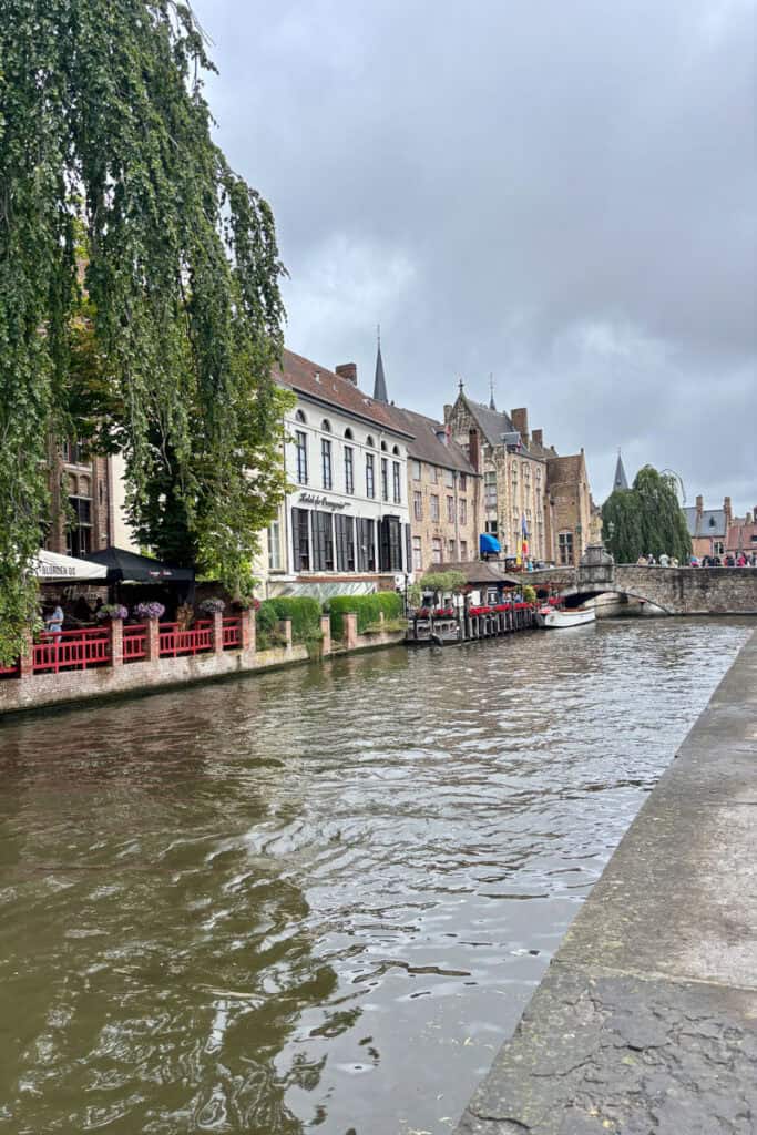 Canal in Bruges with stone bridge and lined by multi-story buildings.