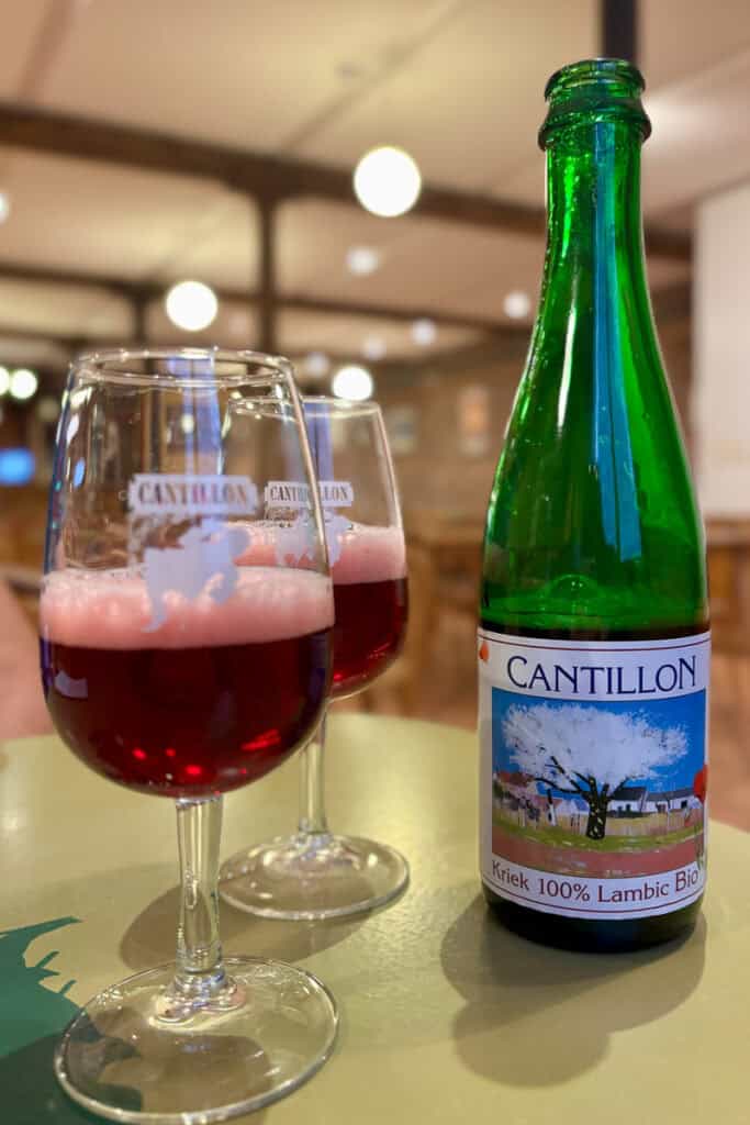 Two glasses of lambic beer next to green bottle with Cantillon Brewery label.