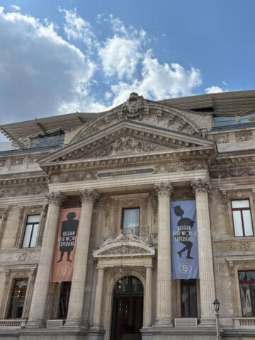 Banners for the Belgian Beer World Experience hanging between the pillars of a tall imposing Roman style building.
