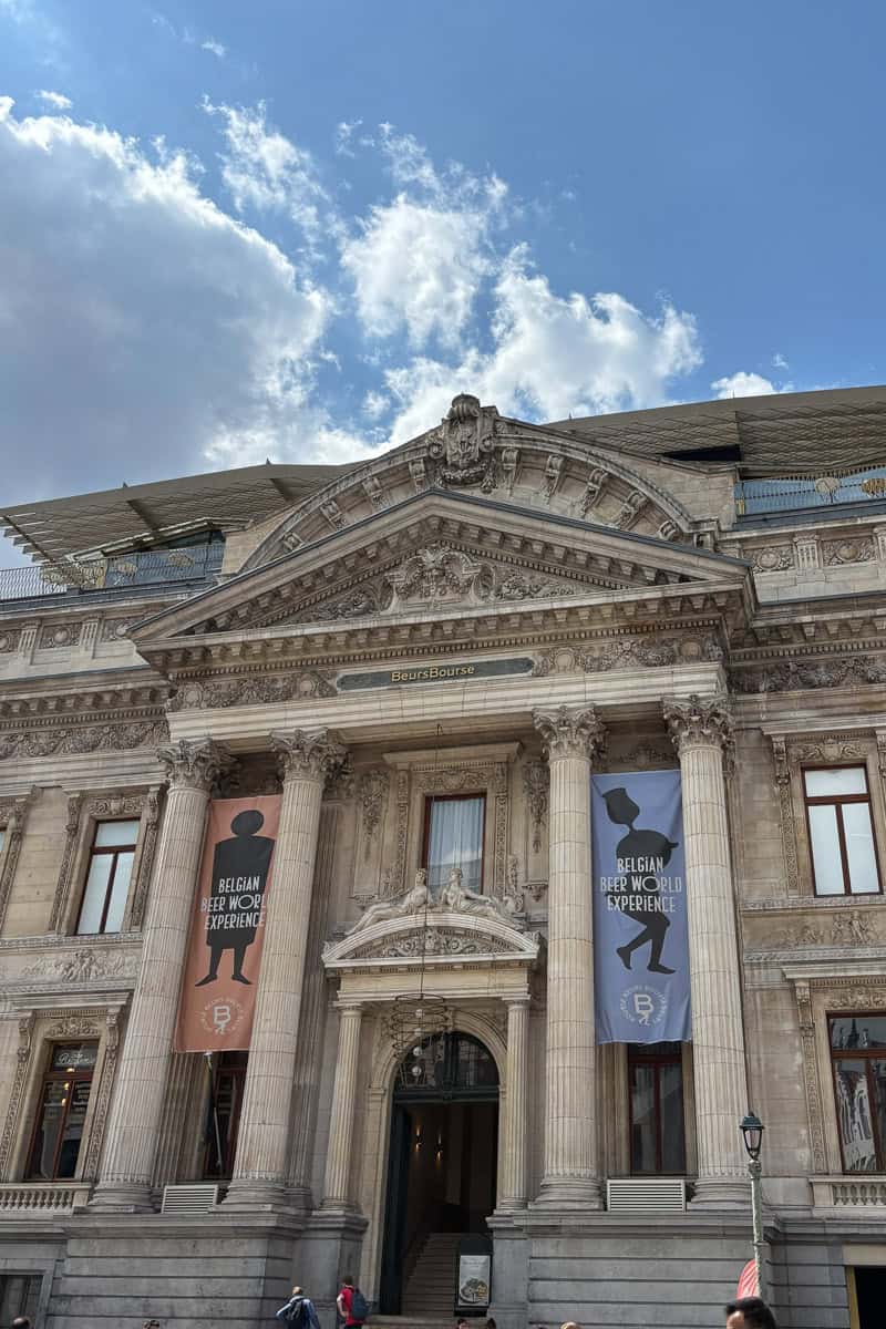Banners for the Belgian Beer World Experience hanging between the pillars of a tall imposing Roman style building.