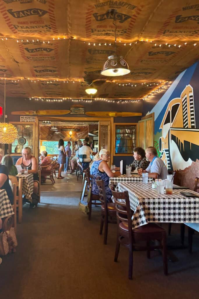 Indoor dining area featuring tables with checkered cloths, rustic light fixtures, and colorful wall murals at Foglight Foodhouse.