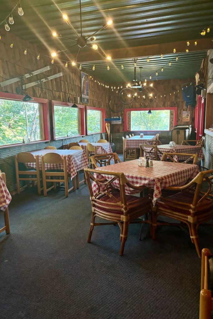 Indoor dining area at Foglight Foodhouse featuring tables with red checkered cloths, wooden chairs, and bulb lighting on strings.