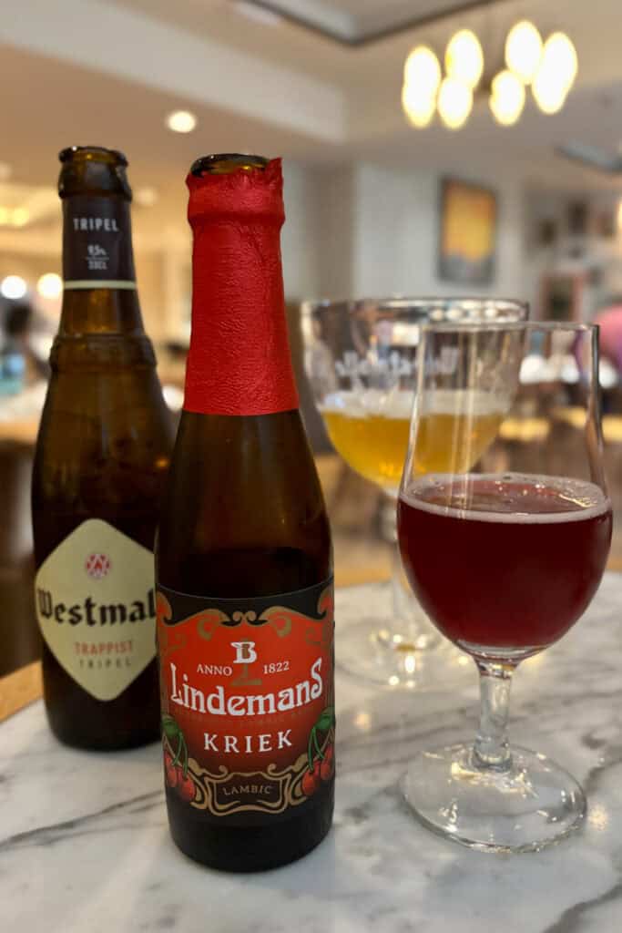 Bottles of lambic and tripel beer with some poured out into glasses.