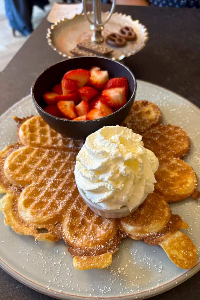 Waffle with a cup of whipped cream and a cup of strawberries.