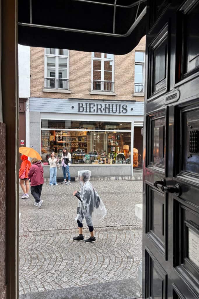 View from The Old Chocolate House across a cobblestone street, with pedestrians dressed for rainy weather.
