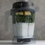 Blender filled with milk, kale, yogurt, peanut butter, protein powder, and frozen fruit to make kale protein smoothie.