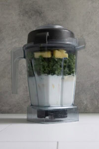 Blender filled with milk, kale, yogurt, peanut butter, protein powder, and frozen fruit to make kale protein smoothie.