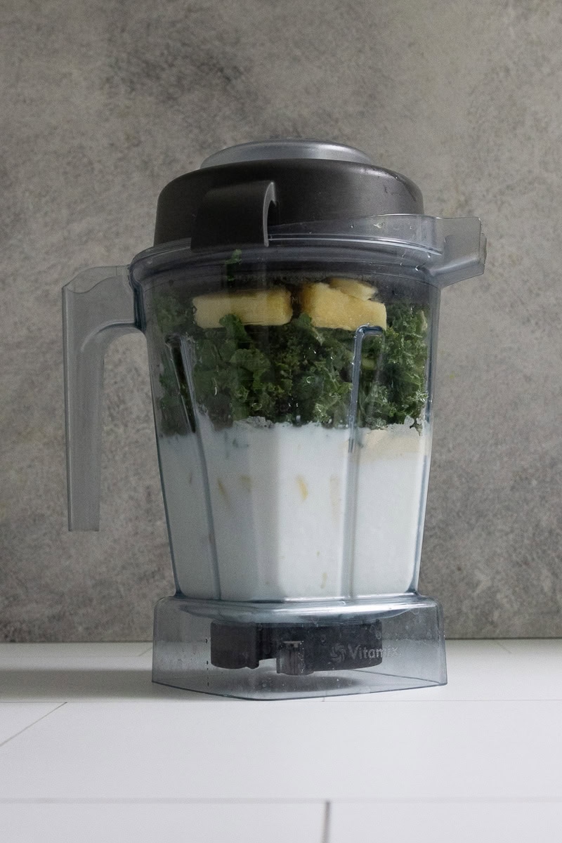 Blender filled with milk, kale, yogurt, peanut butter, protein powder, and frozen fruit to make kale protein smoothie.