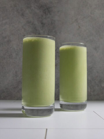 Pale green kale protein smoothie in two tall glasses.