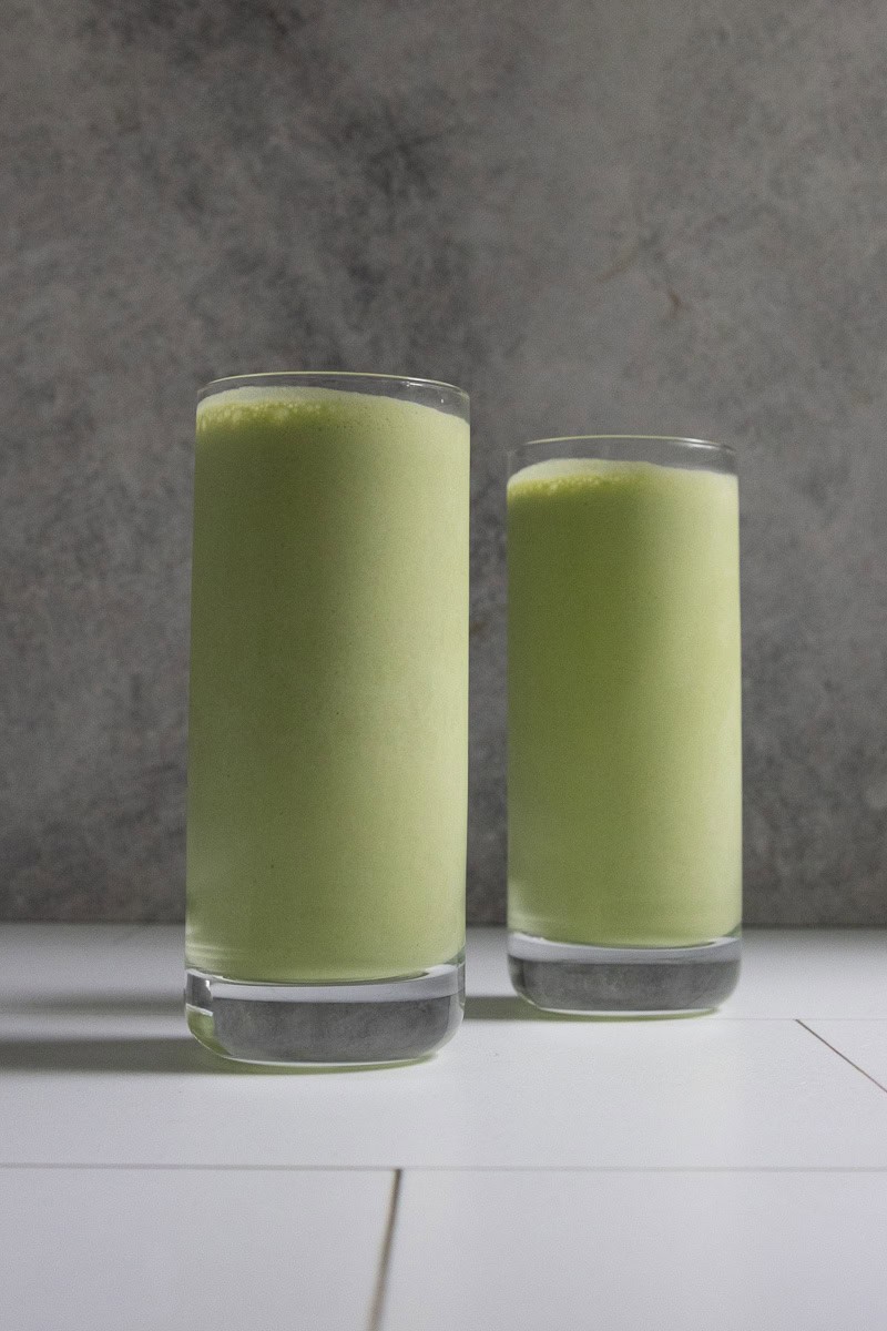 Pale green kale protein smoothie in two tall glasses.
