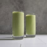Pale green kale protein smoothie in two tall glasses.