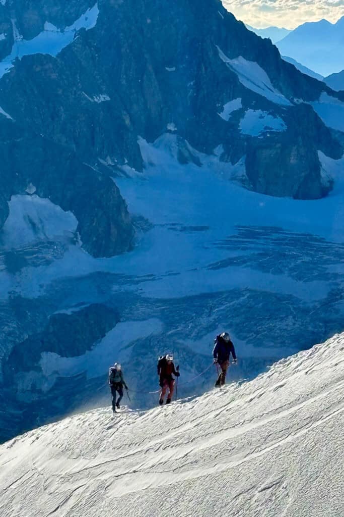 Three mountaineers traversing snowy ridge.