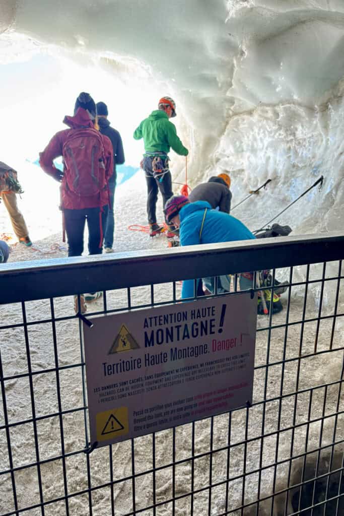 Gate beyond which is mountain access to Aiguille du Midi, and multiple mountaineers beyond it tending to their equipment.