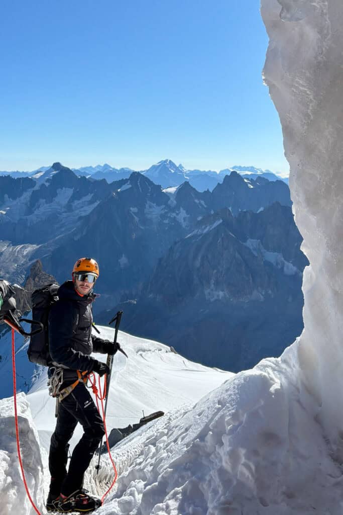 Mountaineer attached to rope and using poles, backpack, helmet, and crampons.
