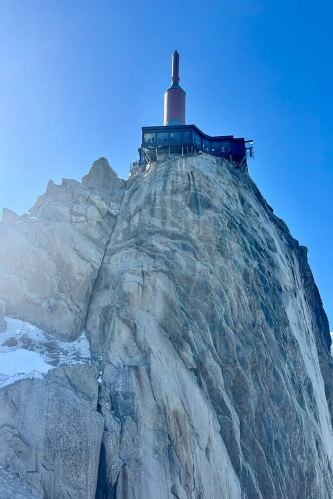 Glare of sun against rocky massif of Aiguille du Midi with viewing area and tower on top.