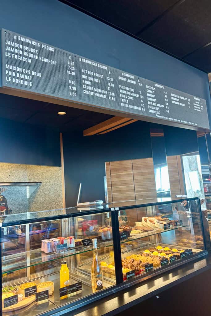 Food choices in glass case and menu board at cafeteria.