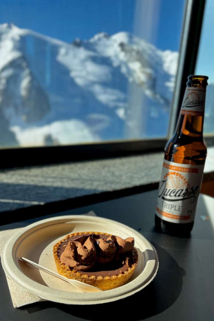 Chocolate mousse tart and bottle of beer next to window overlooking snowy mountain view.